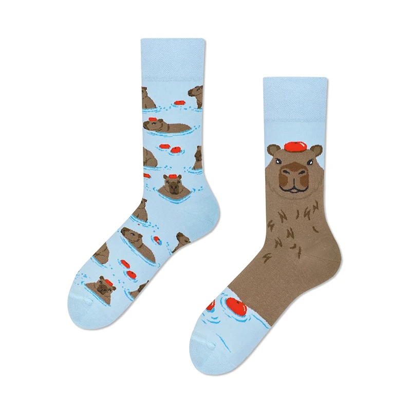 A pair of crew socks featuring a capybara design, with one sock showing the animal in a balancing act pose and the other with a tropical background.
