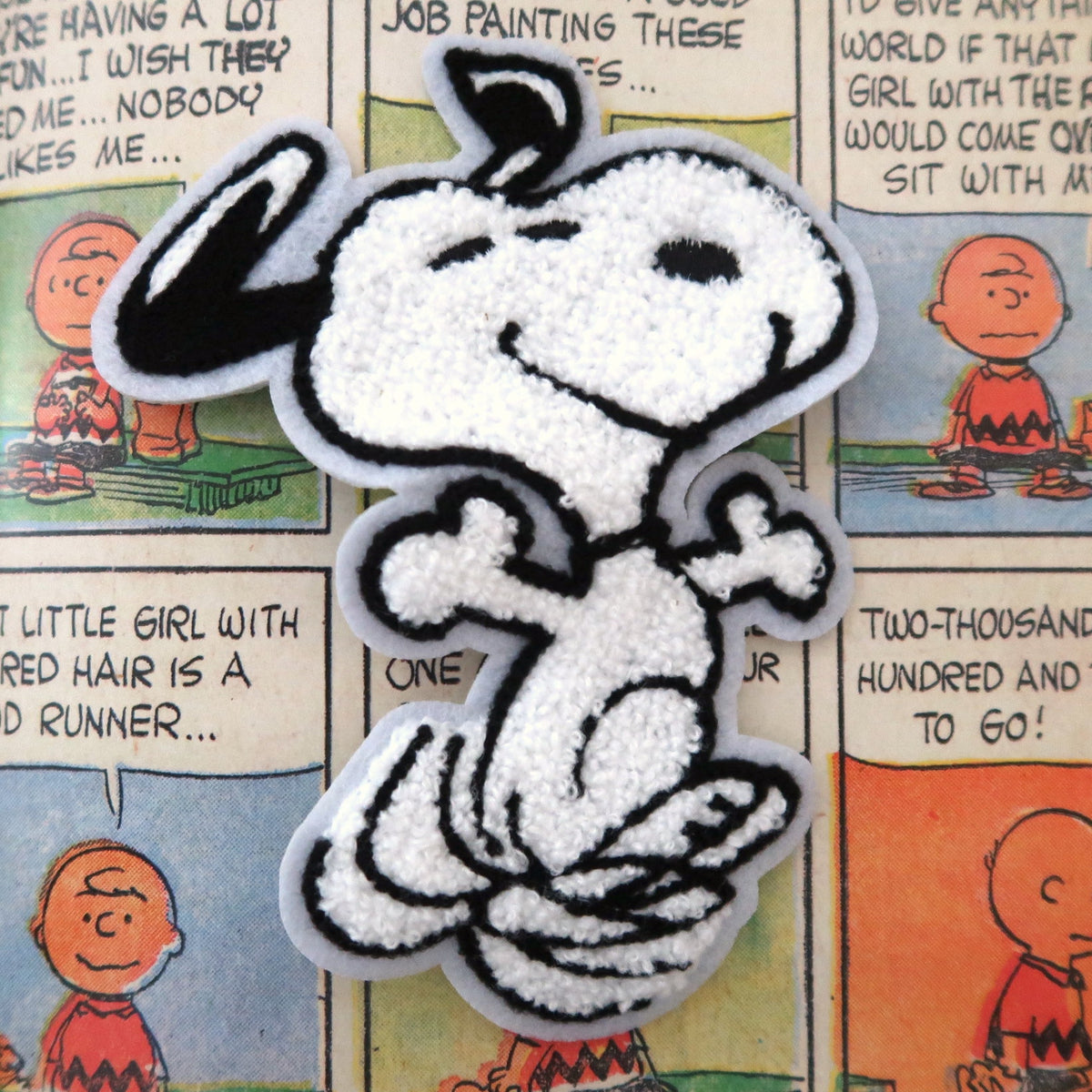 A white and black embroidered patch of Snoopy from Peanuts, displayed on a colorful comic book page background.