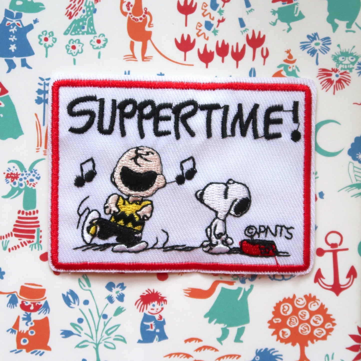 An embroidered patch featuring Snoopy and Charlie Brown from the Peanuts comic strip, with the text 'SUPPERTIME!' and musical notes.