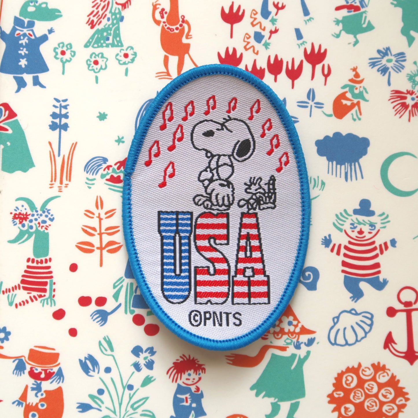A blue-bordered sew-on patch featuring Snoopy from the Peanuts comic strip, with 'USA' lettering, and Woodstock playing the national anthem on a guitar.