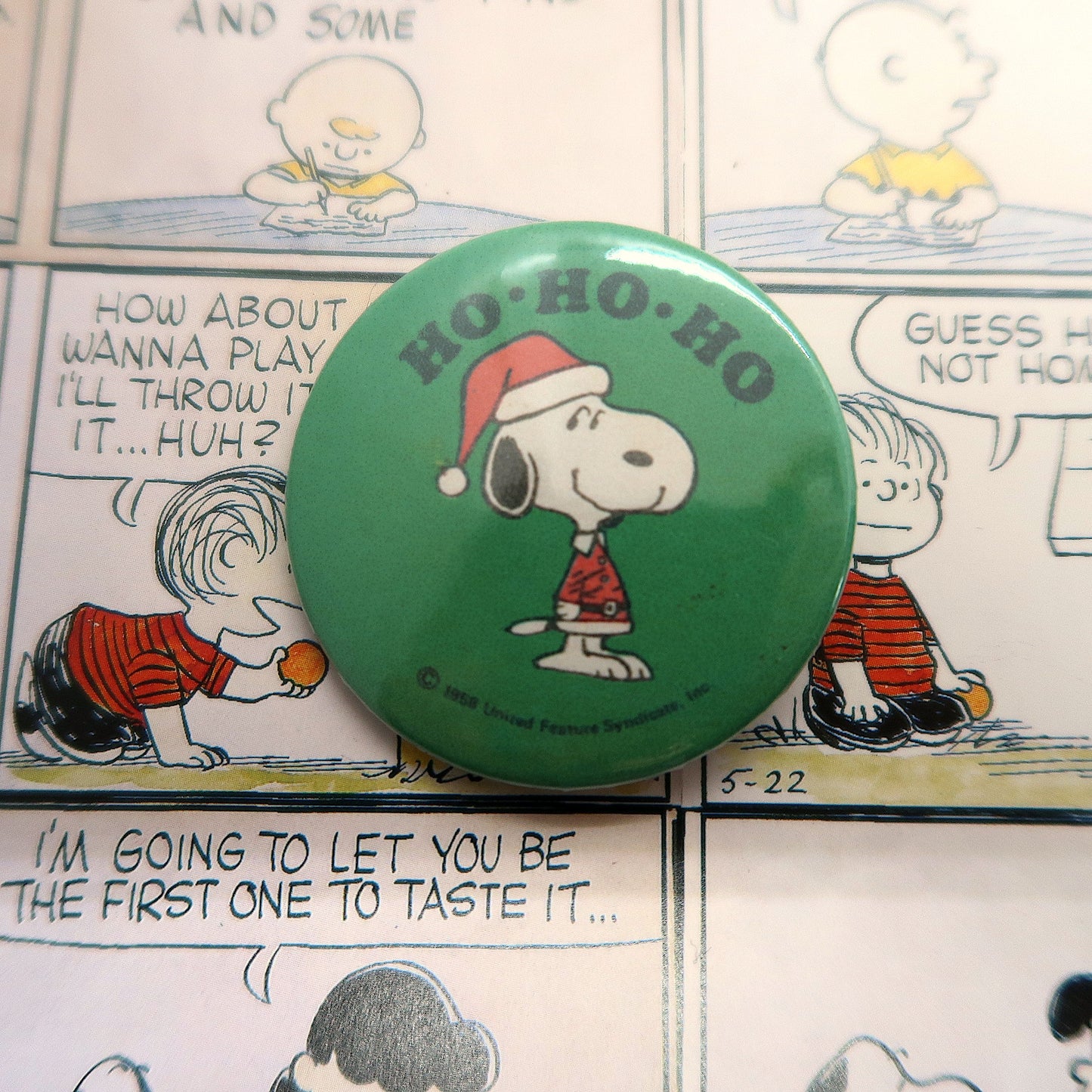 A round pin badge featuring the character Snoopy from the Peanuts comics dressed as Santa Claus with 'Ho Ho Ho' lettering.