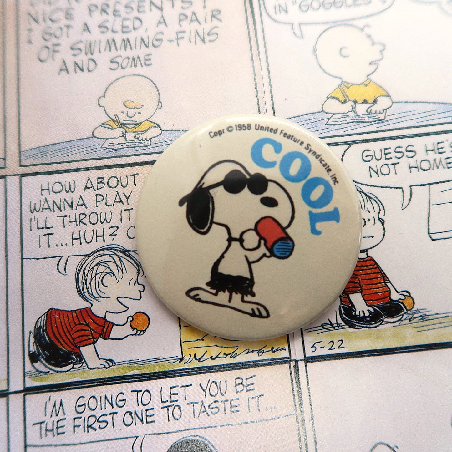 A round pin badge featuring the character Snoopy from the Peanuts comics, wearing sunglasses and holding a can with the word 'COOL' written on it.