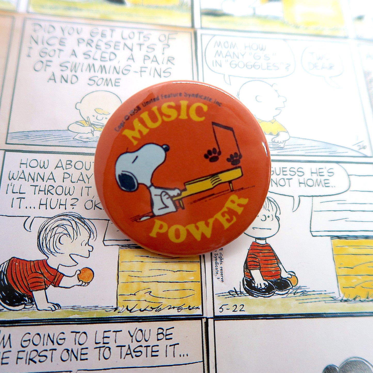 A round orange pin badge featuring the character Snoopy from Peanuts comics playing a piano, with the text 'MUSIC POWER'.