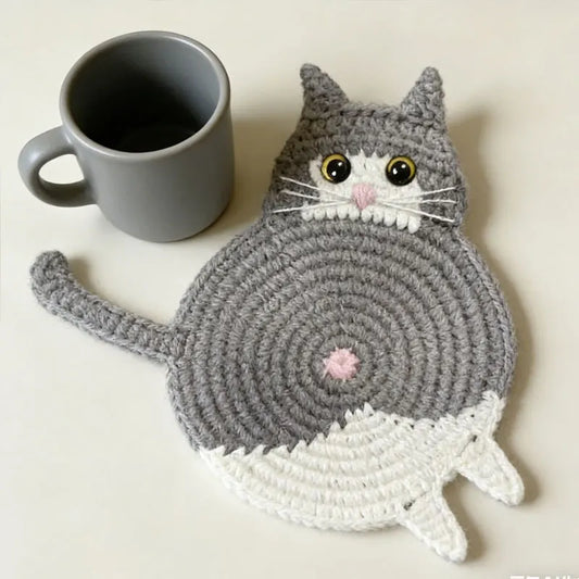Cat-shaped crochet coaster next to a gray mug on a light background