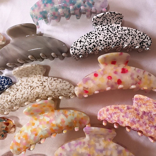 A collection of multicolor and patterned hair claw clips arranged on a soft pink fabric background.