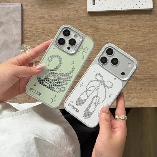 Two phone cases held in hands over a wooden desk. One case is pale mint green with a pixelated swan design, and the other is light gray with a pixelated bow design.
