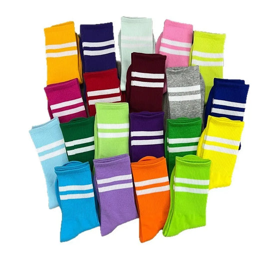 A collection of colorful athletic crew socks with white double stripes near the top, arranged in a pile on a white background.
