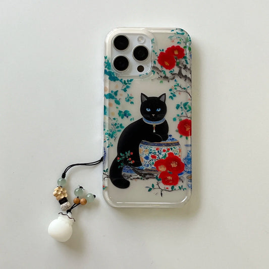 A clear iPhone case featuring a printed design of a black cat sitting on a blue and white patterned teapot surrounded by red flowers, shown on a light gray background with a matching black phone strap charm.