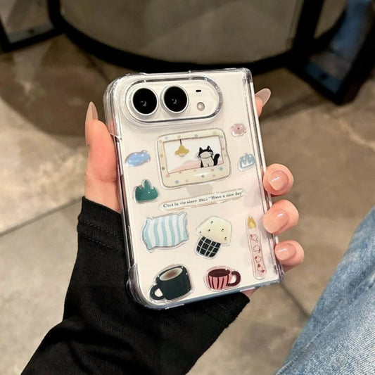 A hand holding a clear phone case decorated with cute pastel illustrations, including a cat in a window, pillows, a mug, and small doodles, shown against a blurred indoor background.