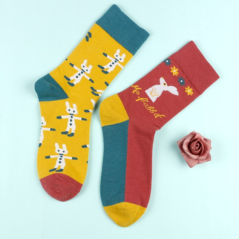 A pair of mismatched crew socks with one featuring a yellow bunny pattern and the other with a red bunny pattern, along with a pink rose and a green bunny logo.