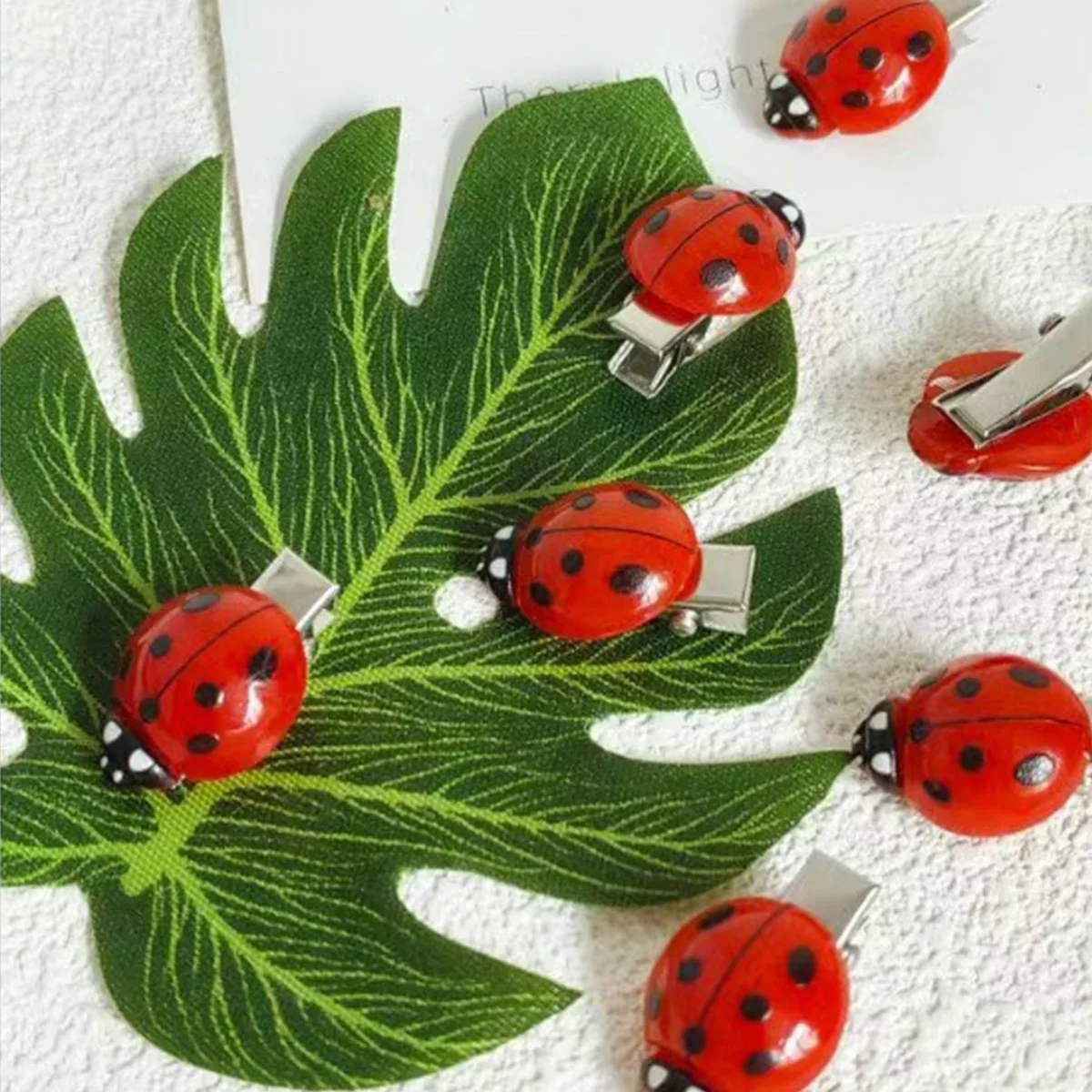 Red ladybug hair clips on a green leaf with a white background