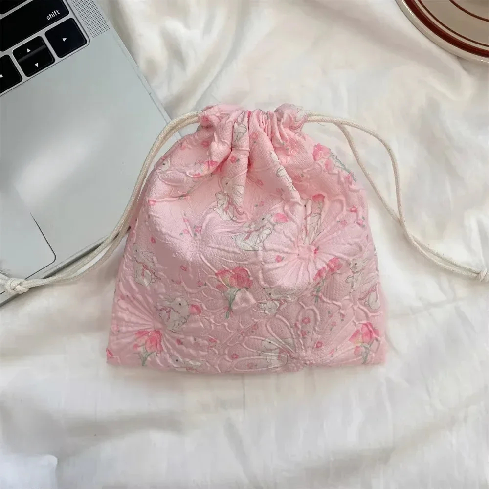 Pink floral drawstring bag on a white surface next to a laptop.