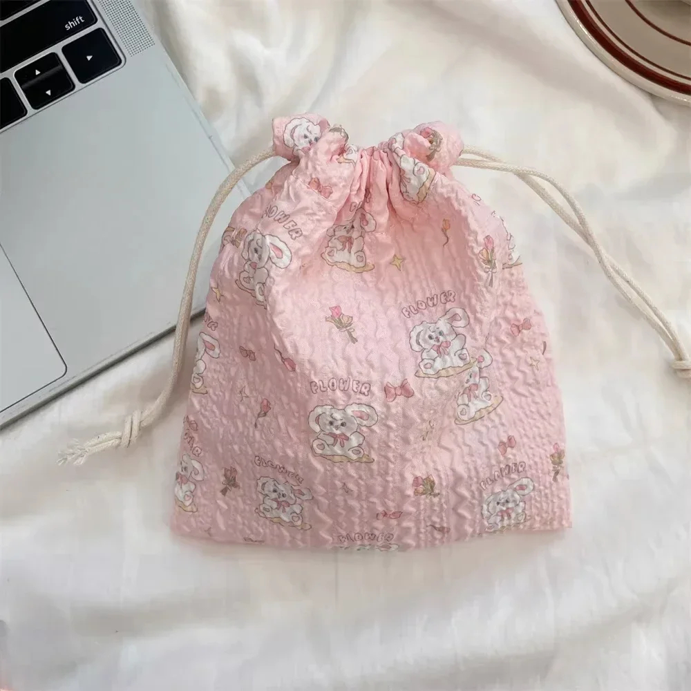 Pink drawstring bag with cartoon designs on a white surface next to a laptop.