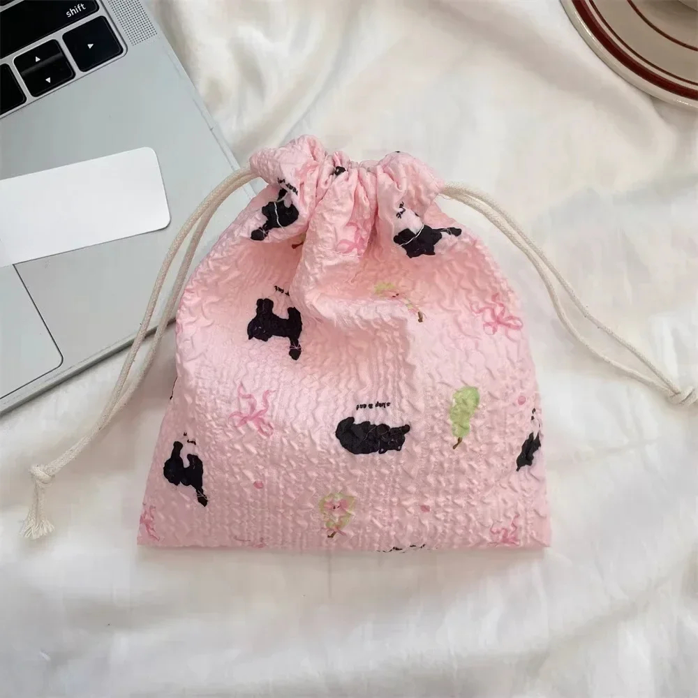 Pink drawstring bag with black and green designs on a white surface next to a laptop.