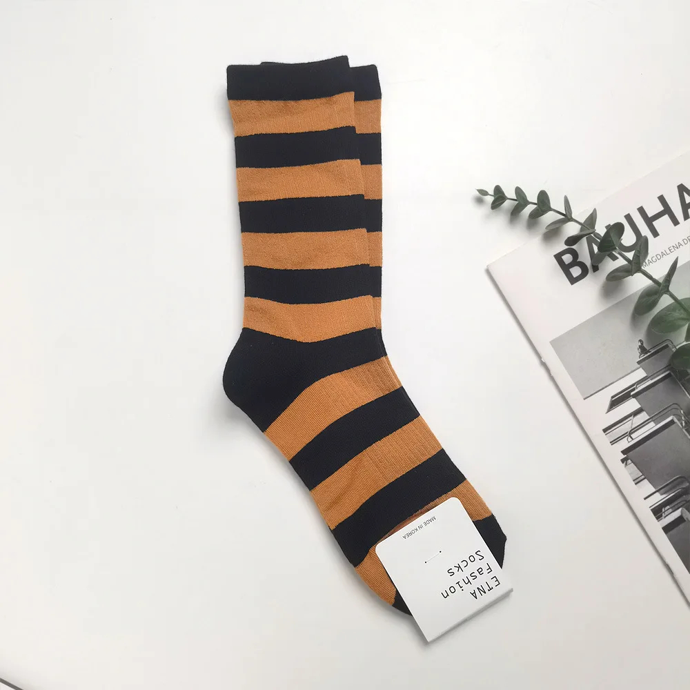 Pair of black and orange striped socks on a white surface with a magazine in the background.