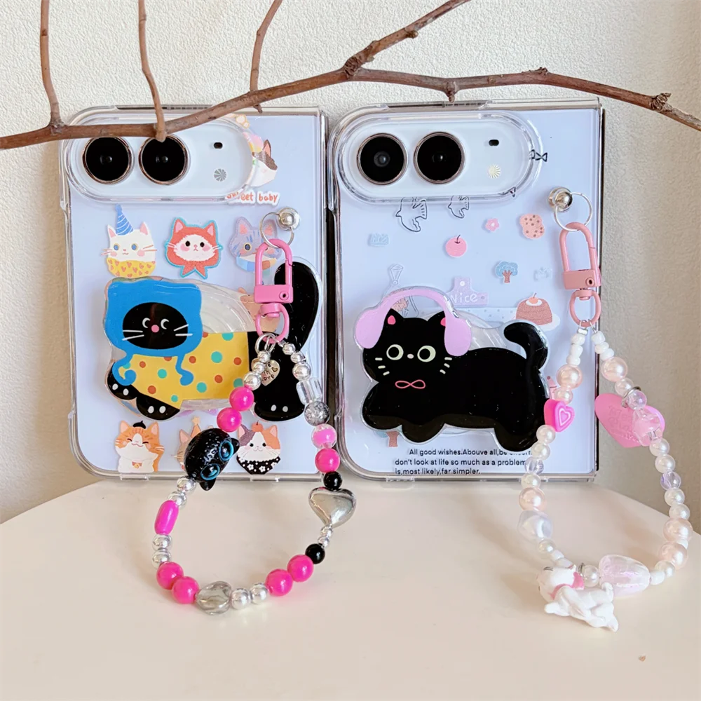 Two clear phone cases with cute cartoon cat designs and attached beaded wrist straps, displayed on a light surface with a decorative branch behind them.