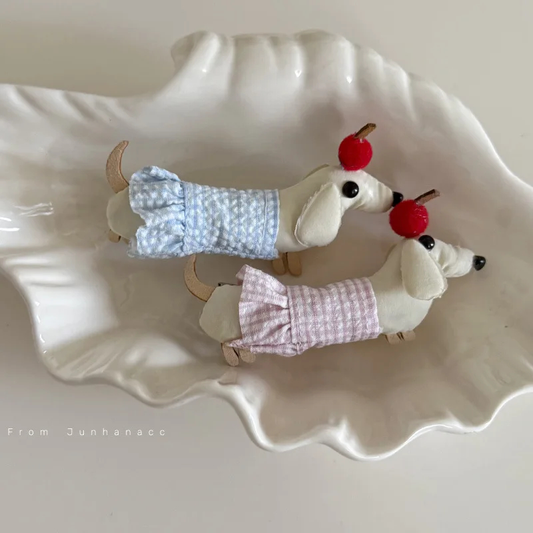 Two small dog figurines wearing dresses on a decorative plate.