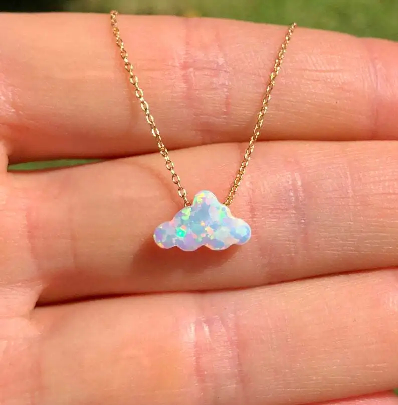 Opal cloud-shaped pendant on a gold chain held between fingers with a blurred green background