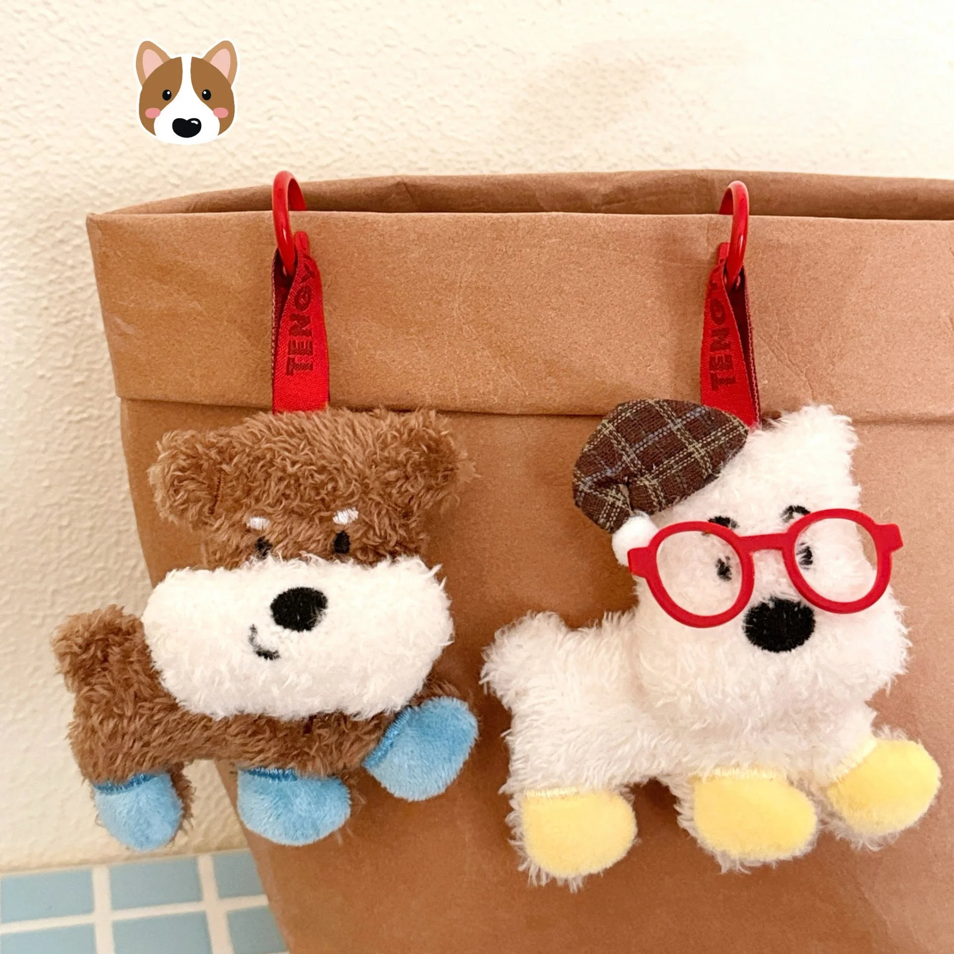 Two plush toys, a brown dog and a white dog with glasses, hanging from a brown bag.