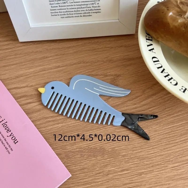 Bird-shaped comb with clip on a wooden surface next to a pink book and a white plate with a roll of bread.