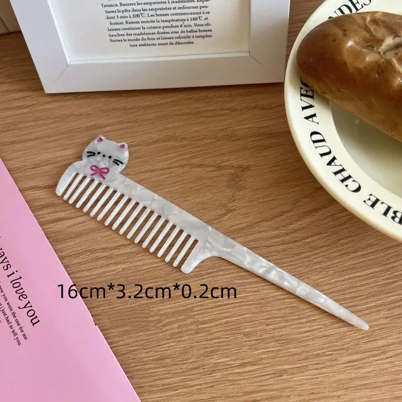 Cat-shaped comb on a wooden surface with a pink book and a white plate with bread in the background.