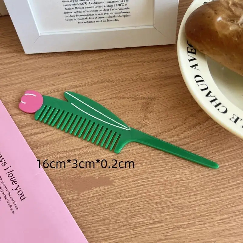 Green tulip comb with pink top on a wooden surface next to a pink book and a white plate with a loaf of bread.