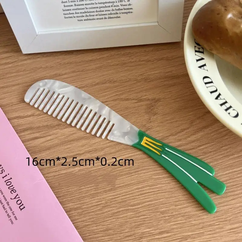 Small leek comb with green handle on a wooden surface next to a pink book and white dish.