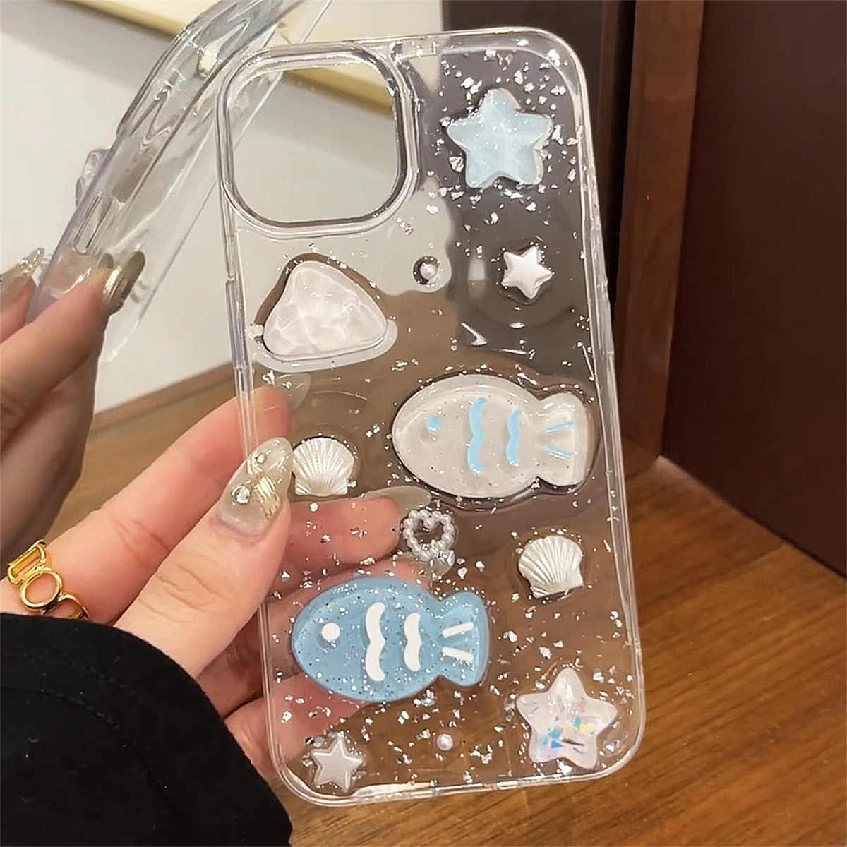 Clear phone case with fish and star designs held by a hand.