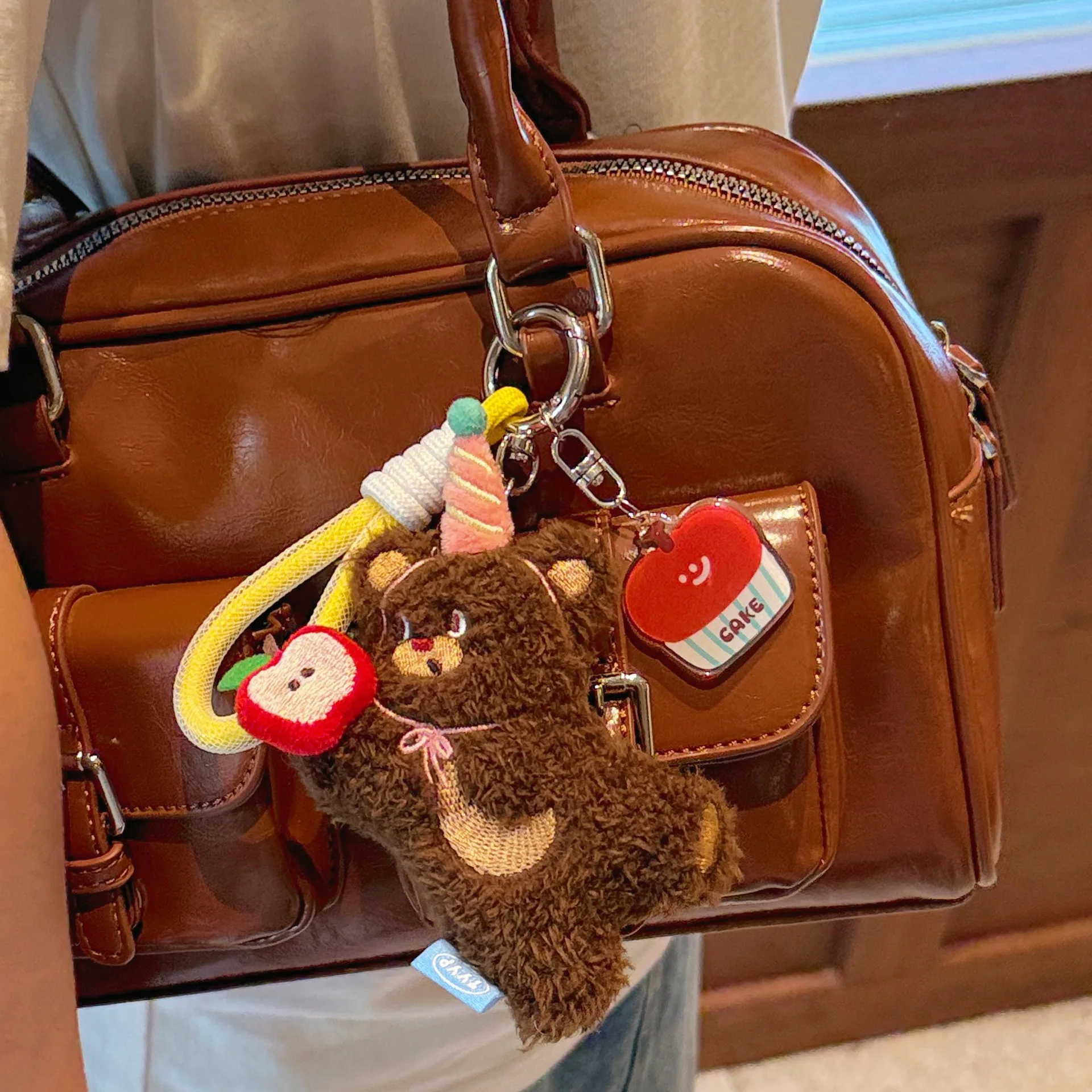 Brown teddy bear keychain with heart-shaped tag attached to a brown handbag.