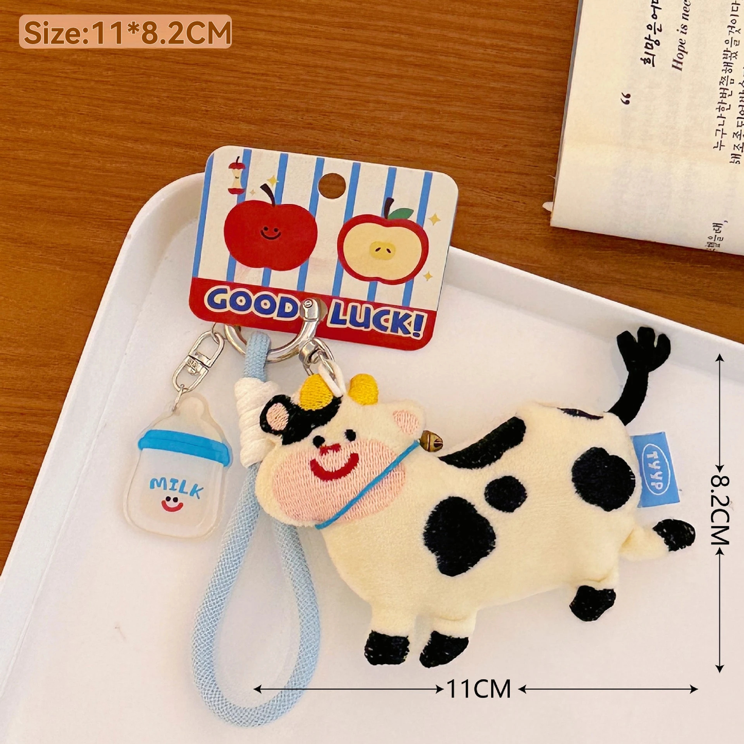 Plush cow keychain with a 'Good Luck!' tag on a white tray