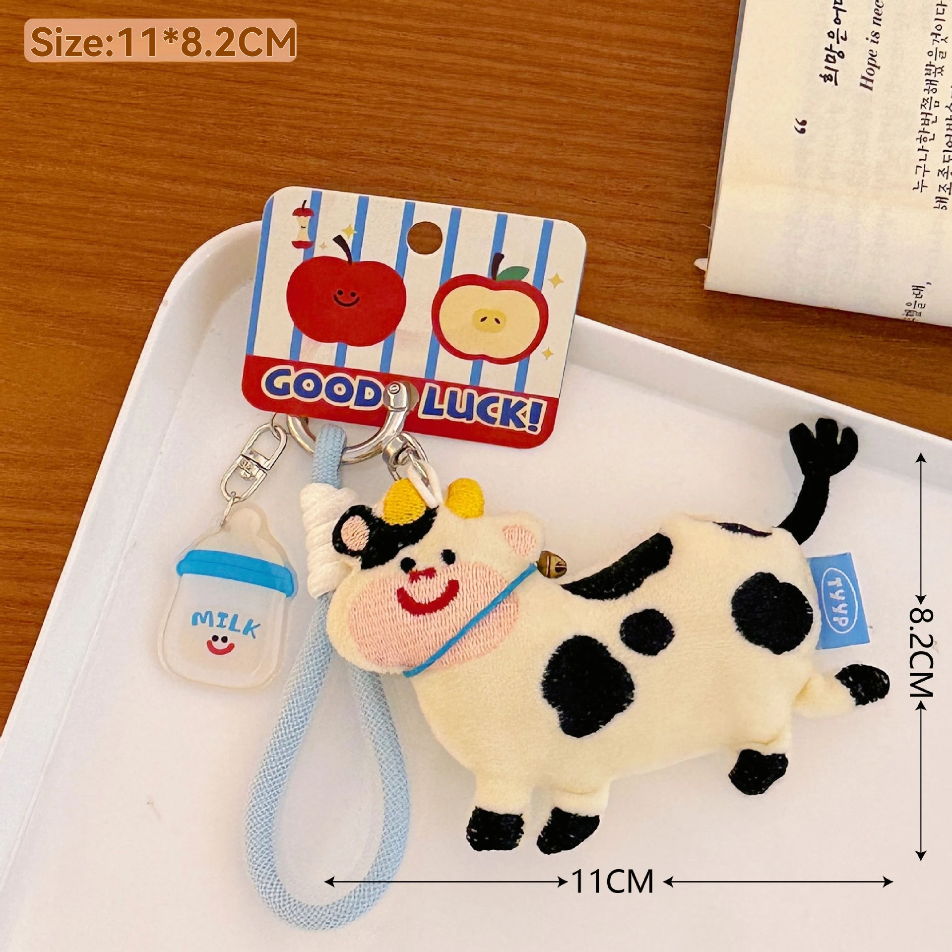 Plush cow keychain with a 'Good Luck!' tag on a white tray
