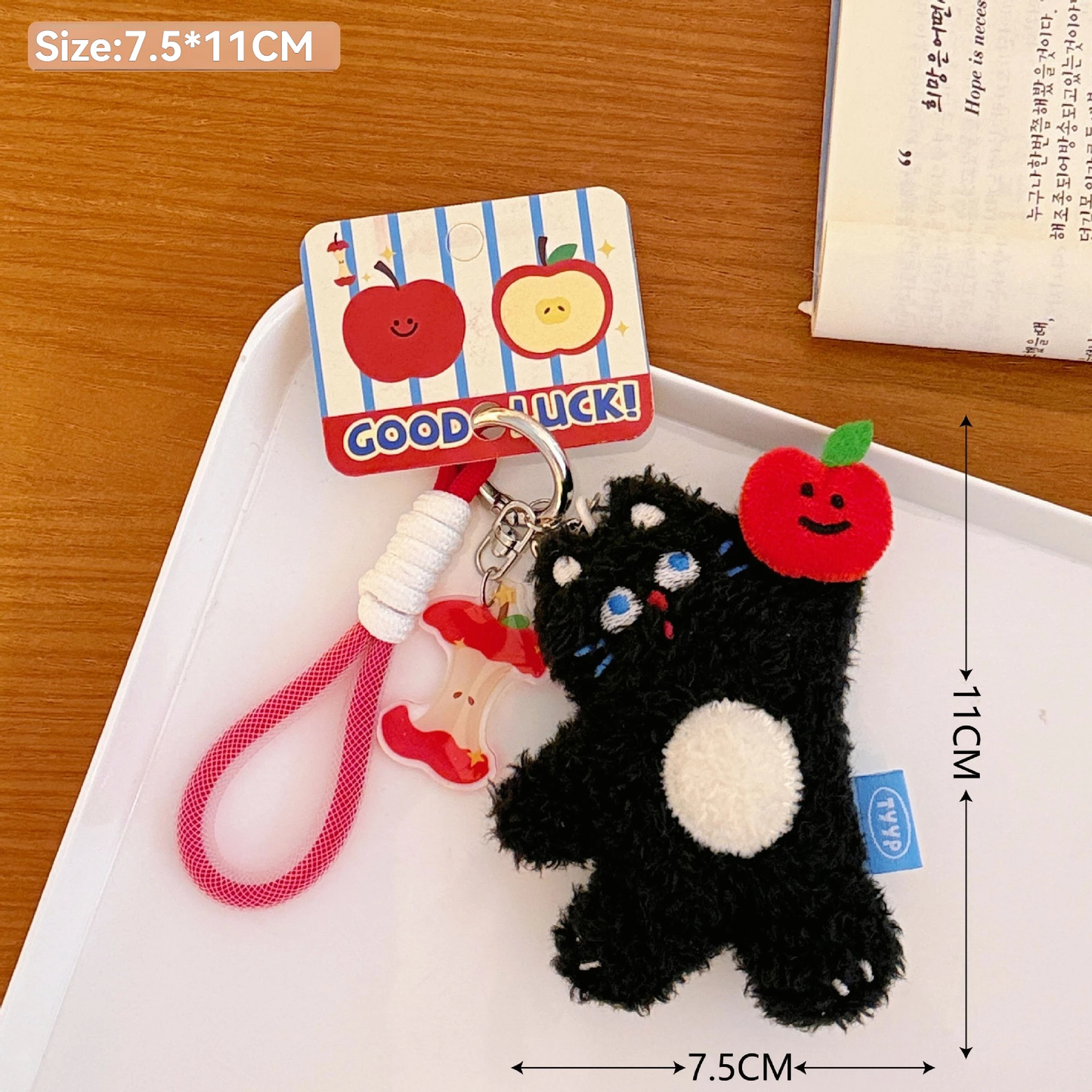 Black cat plush keychain with red apple decorations on a white tray, with dimensions indicated.