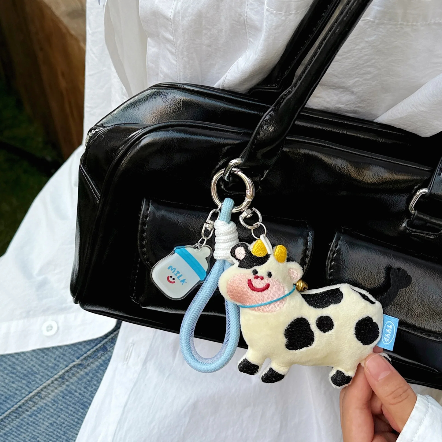 Cow-shaped keychain with a blue strap attached to a black bag.