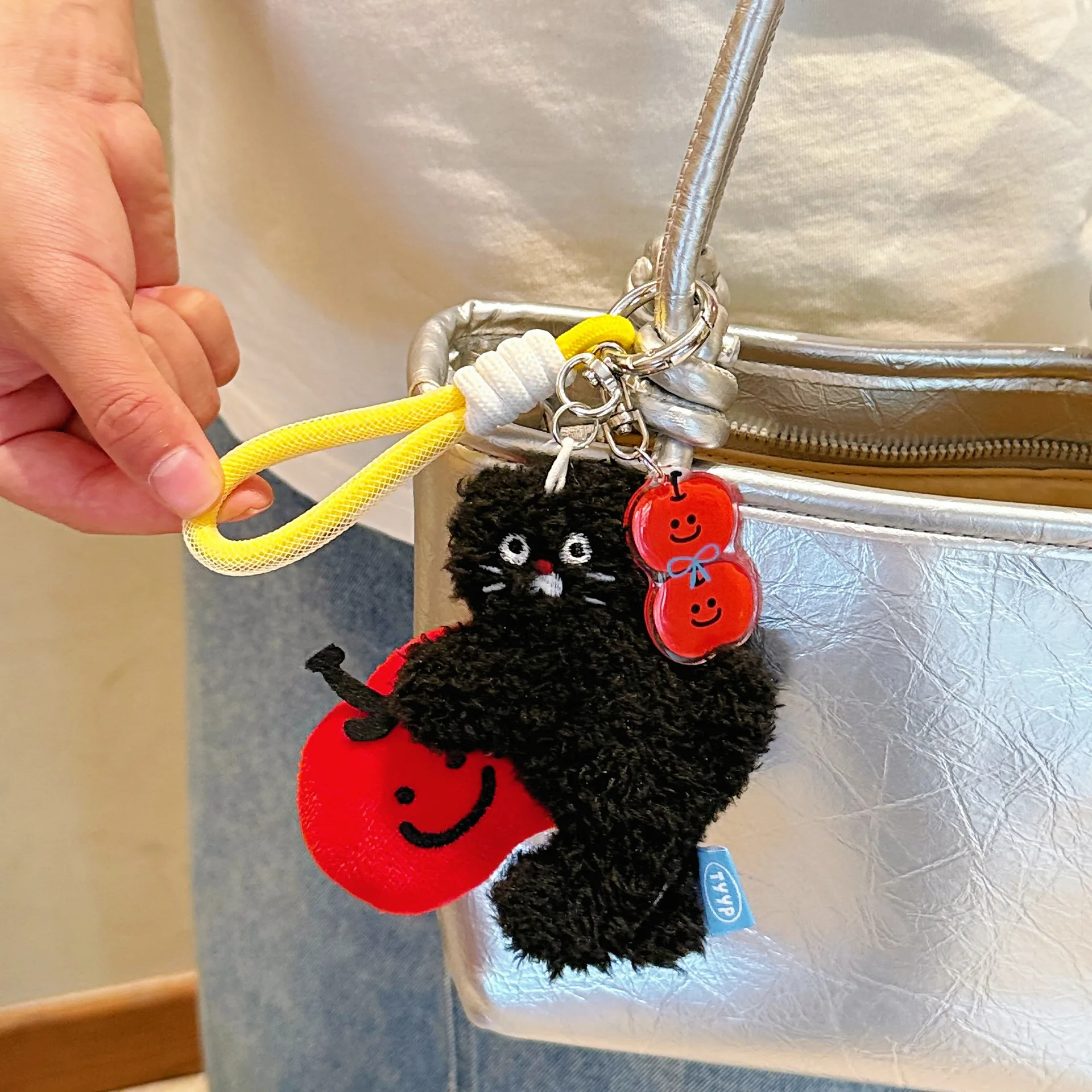 Black cat keychain with red apple charm attached to a silver bag.