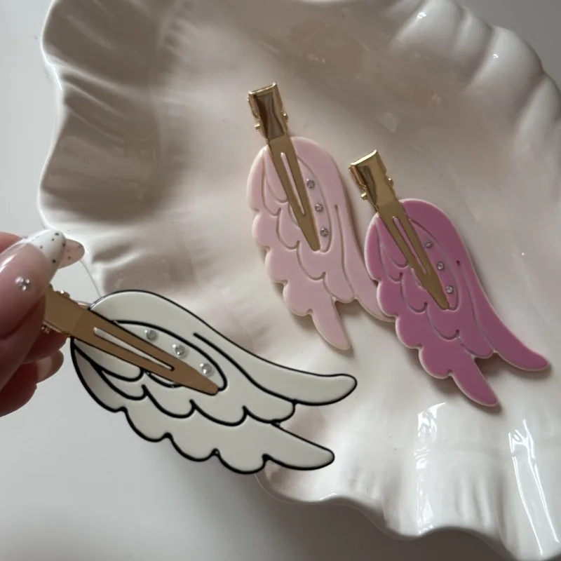 Decorative hair clips shaped like angel wings on a white dish.