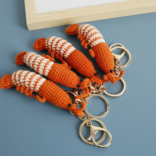 Crocheted shrimp keychain with gold rings on a blue surface