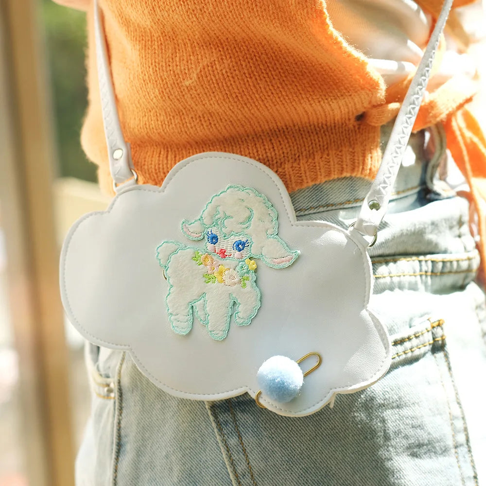 White cloud-shaped bag with embroidered design held by a person wearing an orange sweater and denim jeans.