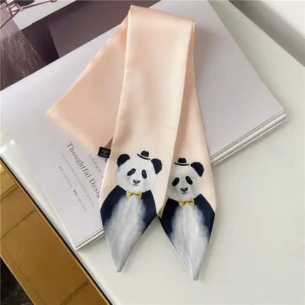 A pale blush pink silk necktie with two printed panda illustrations at the pointed ends, styled on top of a white notebook.
