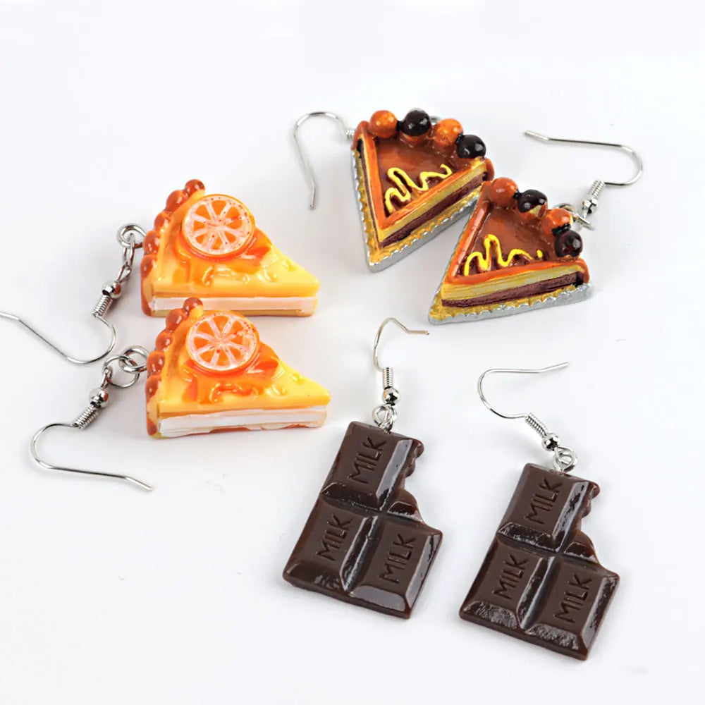 Dessert-themed earrings including cake slices and chocolate bars on a white background