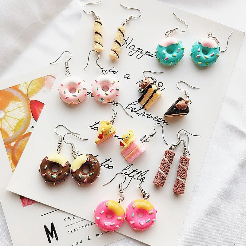 Various colorful earrings shaped like donuts, pizza slices, and other food items on a white surface.