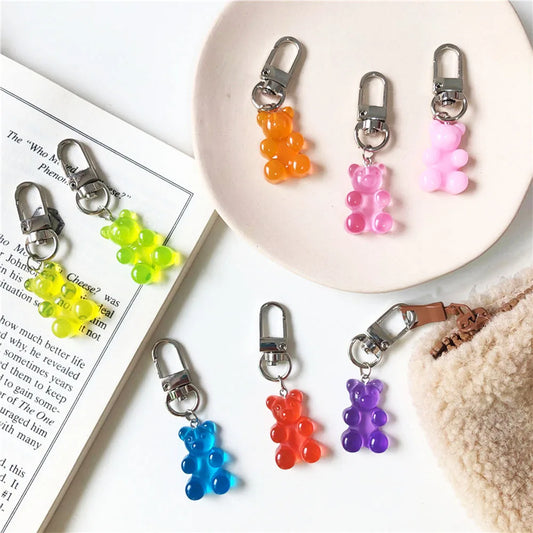 Colorful gummy bear keychains on a white surface with a book and fur blanket.