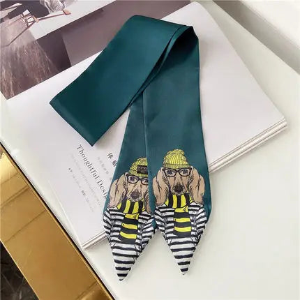 A dark teal satin necktie with a humorous cartoon print of two dogs dressed as thieves, featuring yellow hats, striped scarves, and black-and-white striped tails, displayed on a white book.