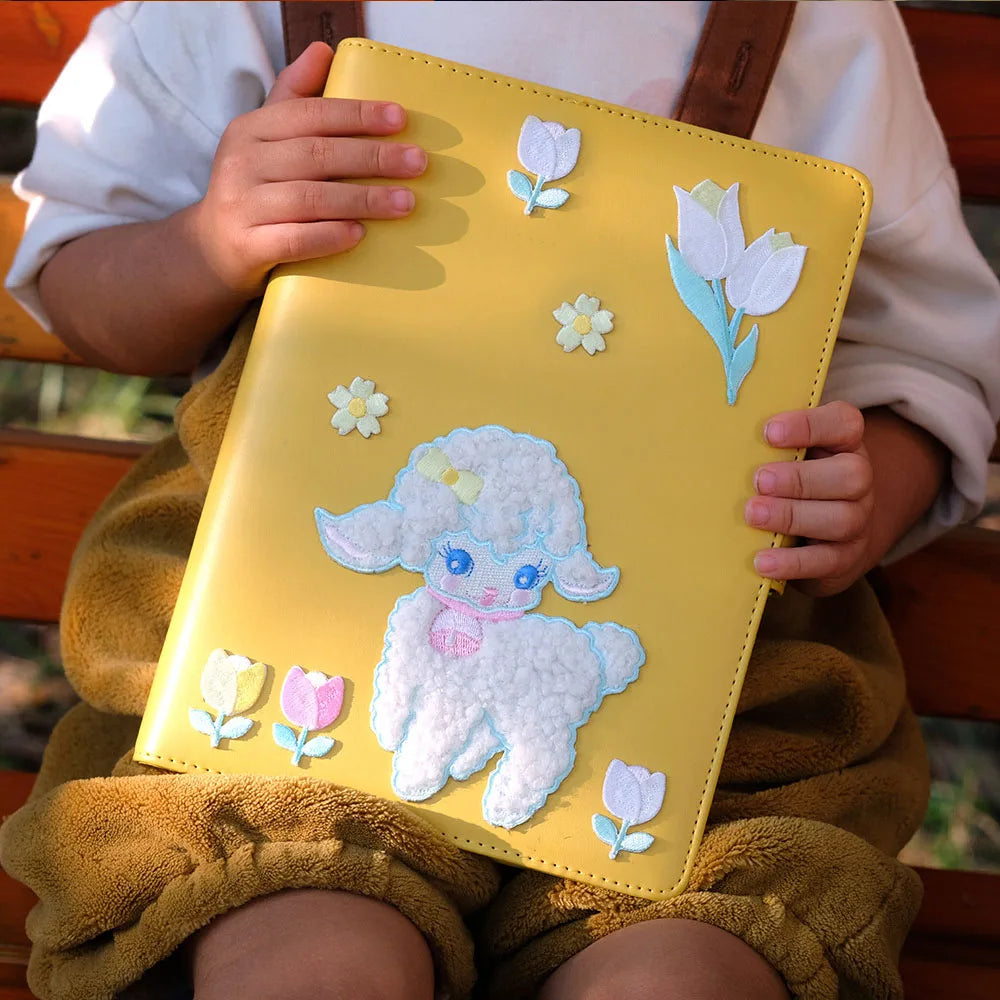 Person holding a yellow notebook with a lamb and flower design.