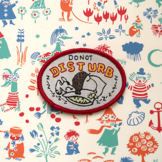 A cream-colored embroidery patch with a red border featuring the character Snoopy from the Peanuts comic strip, with 'Do not Disturb' lettering, and various colorful background characters.