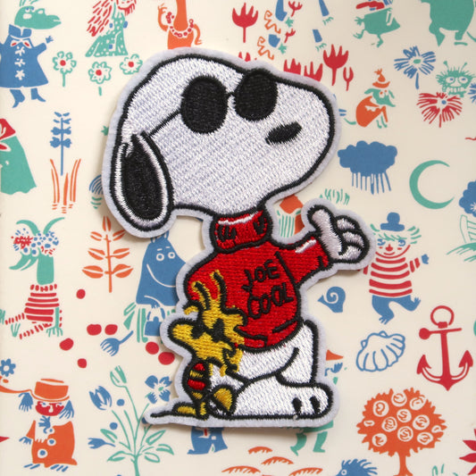 An embroidered iron-on patch featuring Snoopy and Woodstock from the Peanuts comics, with the characters wearing sunglasses and a red turtleneck sweater, sitting on a graphic background.