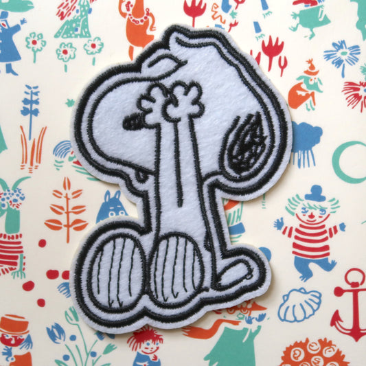 A black and white embroidered patch featuring the character Snoopy from the Peanuts comic strip, with the patch depicting Snoopy covering his eyes and saying 'Peek-a-boo'.