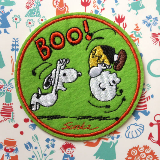 A green round embroidered patch featuring Snoopy and Charlie Brown from the Peanuts comic strip, with the word 'Boo!' and a scared facial expression.