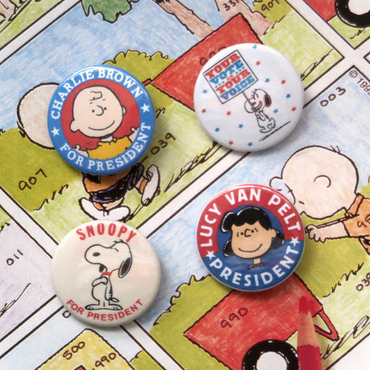 A set of four vintage style pin badges featuring Snoopy and other characters from Peanuts comics with presidential election themes.
