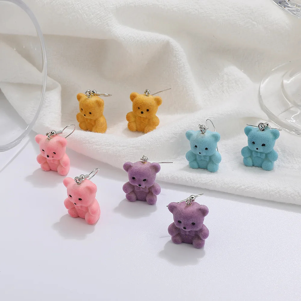 Set of colourful flocked teddy bear-shaped earrings on a white fabric background