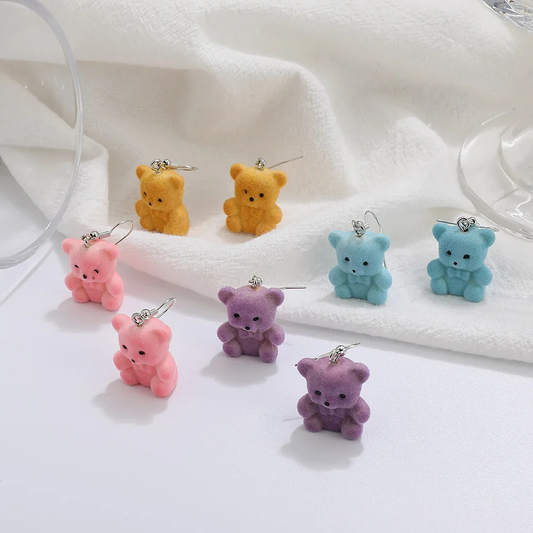 Set of colourful flocked teddy bear-shaped earrings on a white fabric background
